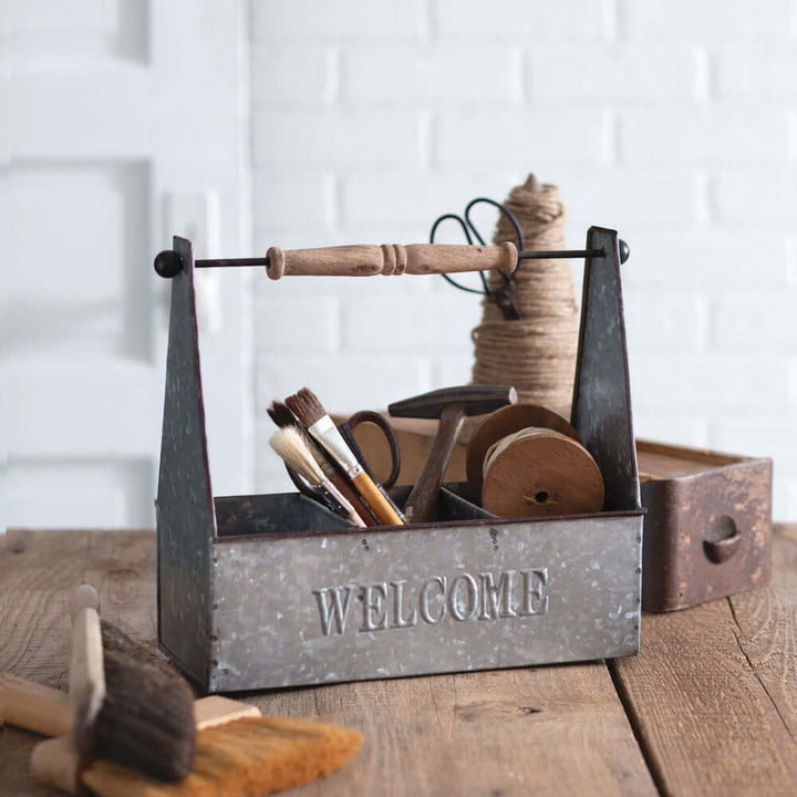 Rustic farmhouse kitchen caddy with welcome sign, holding tools and paper towels on a wooden table.