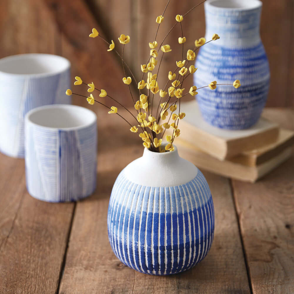 Blue and white textured ceramic bud vase with yellow flowers, surrounded by additional ceramic vases on a wooden surface.