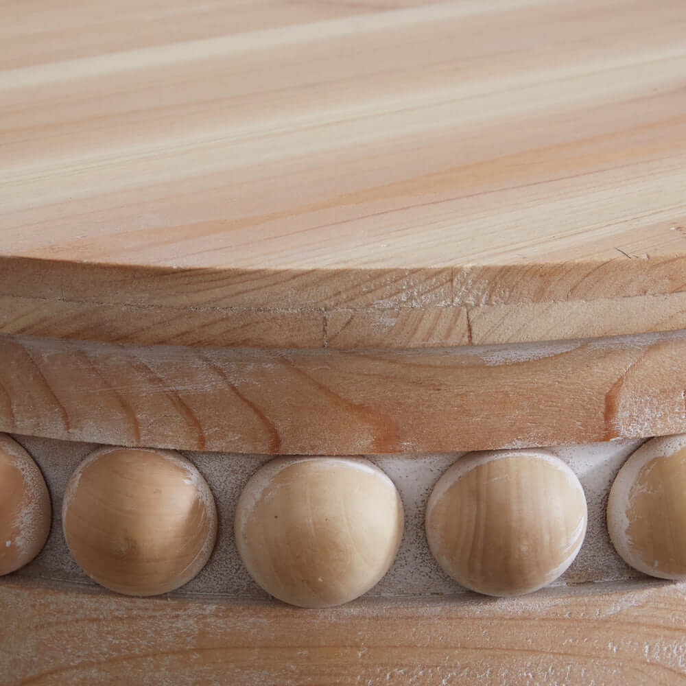 Close-up of the natural wood top and decorative bead detailing on a round Boho side table.