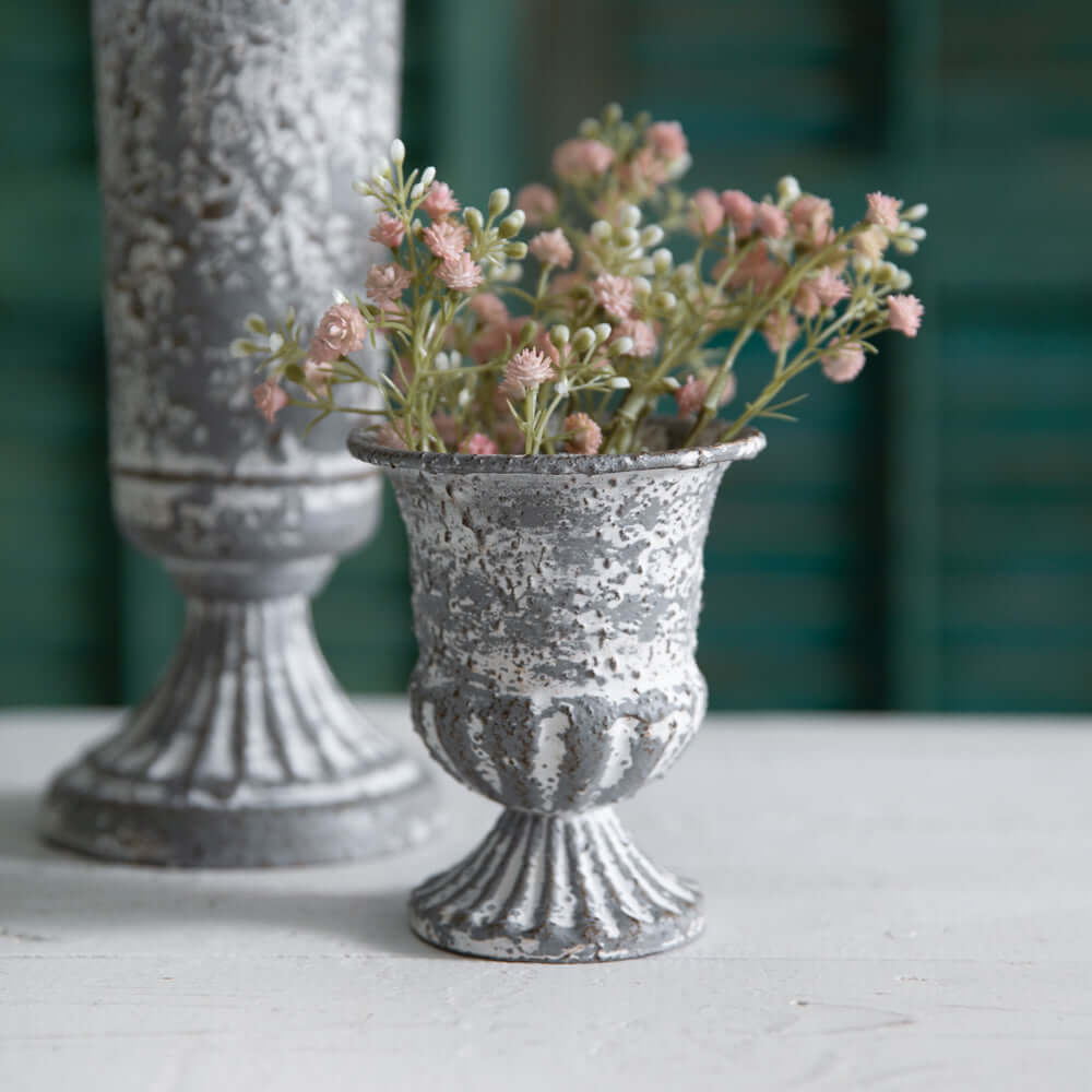 Antique farmhouse metal urn with pink flowers, showcasing vintage charm and rustic elegance.