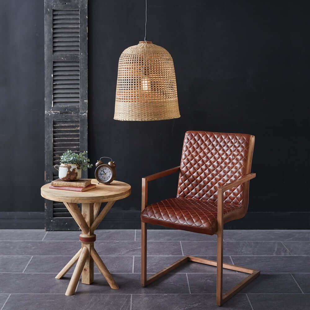 Bohemian handwoven grass pendant lamp above a stylish brown leather chair and wooden side table in a modern interior setting.