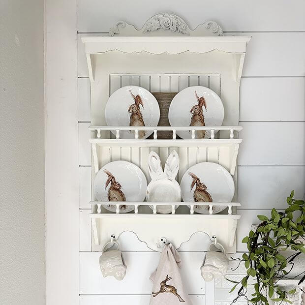 French country wall-mounted dish rack with decorative plates featuring bunnies, enhancing rustic kitchen decor.