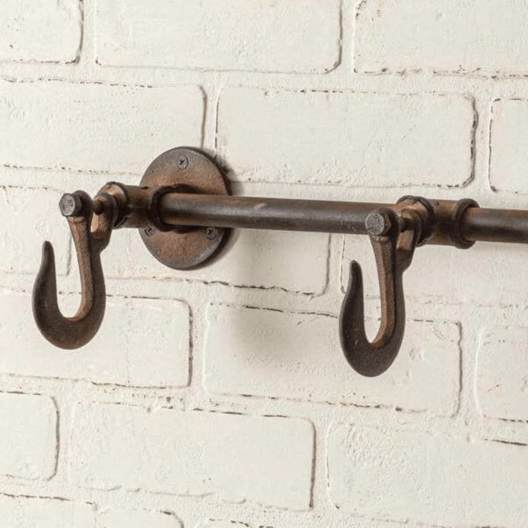 Industrial three hook wall rack with cast iron finish mounted on white brick wall, ideal for farmhouse or vintage decor.