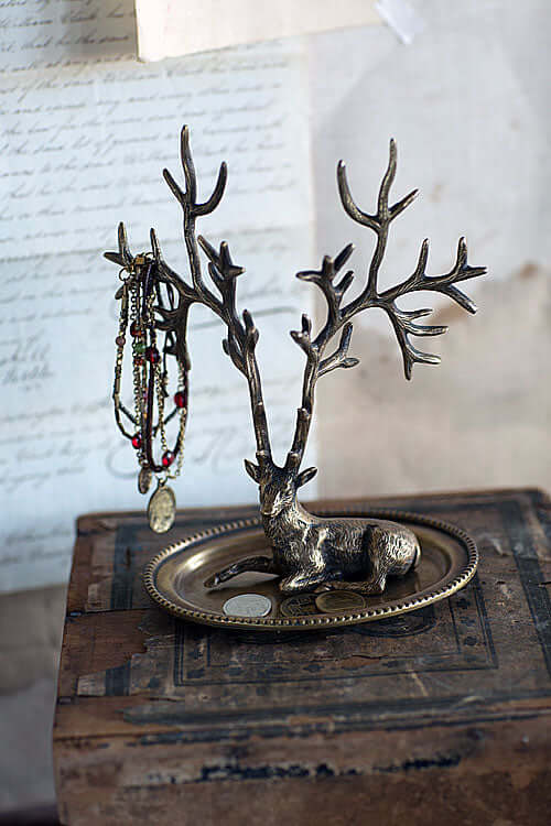 Antique brass deer jewelry holder with intricate antlers and jewelry elegantly displayed on a vintage-style tray.