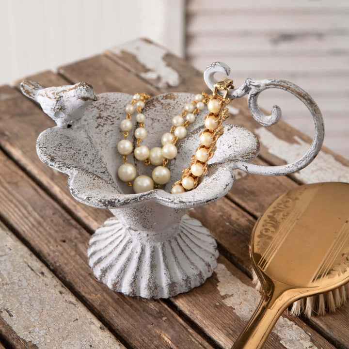 Rustic cast iron bird feeder with flower basin and bird figurine, adorned with vintage-inspired necklaces, on wooden surface.