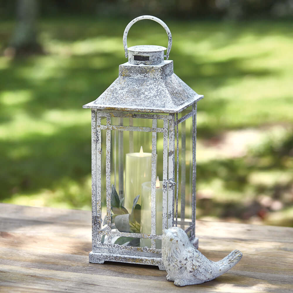 Rustic farmhouse lantern in weathered metal with candle, perfect for indoor or outdoor decor.