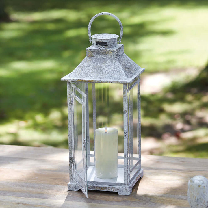 Rustic farmhouse lantern in weathered metal with a candle, perfect for indoor or outdoor decor.