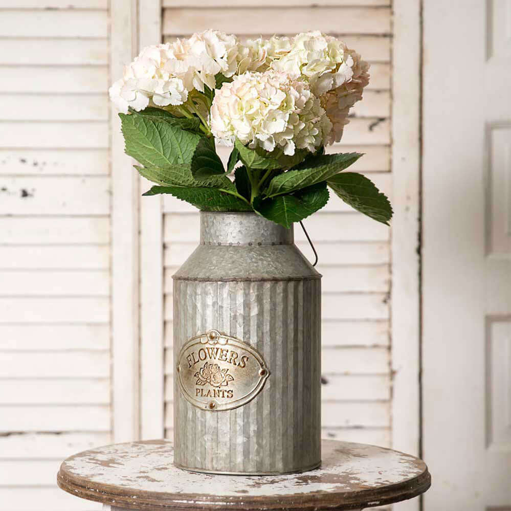 Rustic galvanized metal vase with embossed label, filled with hydrangeas, adding farmhouse charm to home décor.