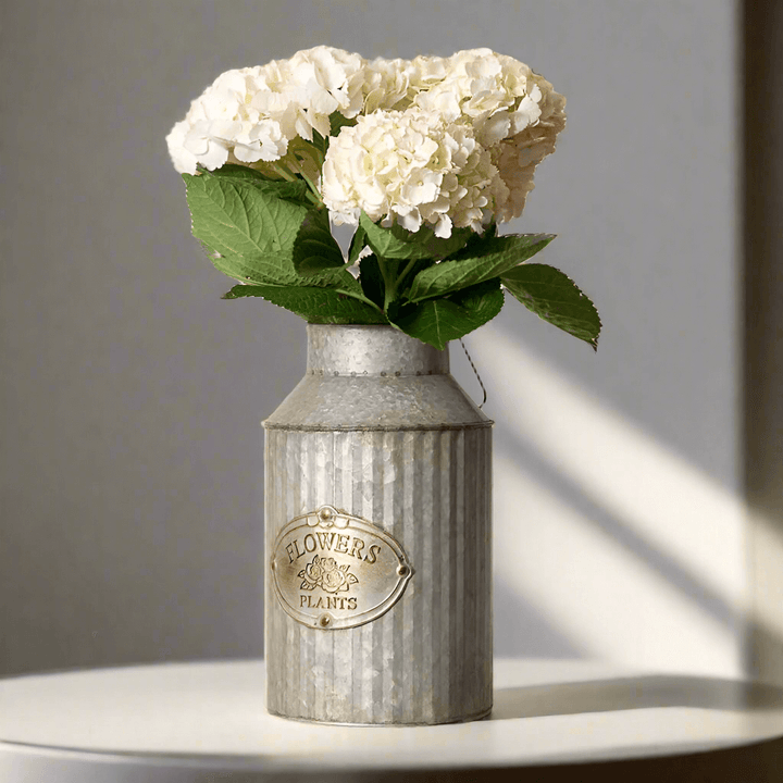 Rustic galvanized metal vase with "FLOWERS PLANTS" label holding white hydrangeas, perfect for farmhouse decor.