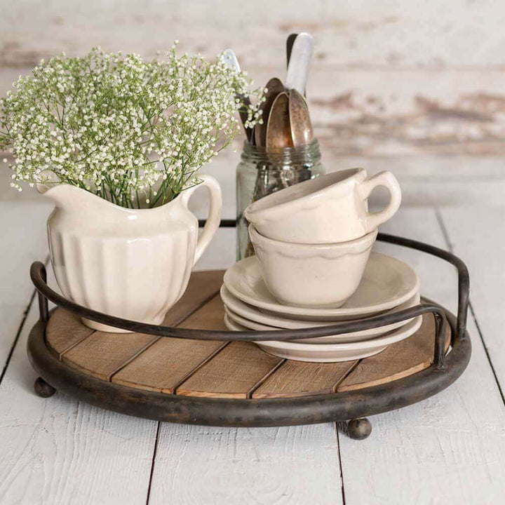 Rustic round wood tray with metal handles displaying white dishes and a vase of flowers, perfect for vintage decor.