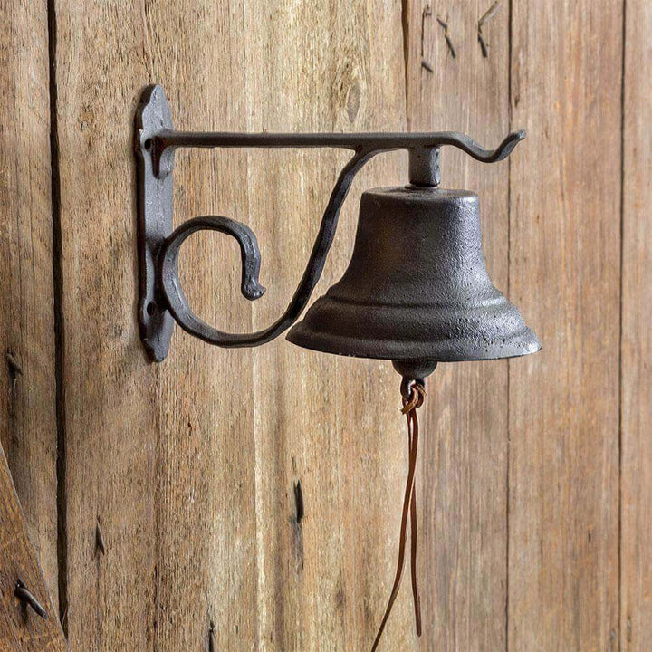 Vintage wall-mounted farmhouse bell in cast iron against rustic wooden background, perfect for home or garden decor.