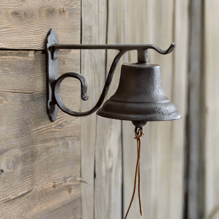 Vintage wall-mounted farmhouse bell in cast iron, elegantly designed for rustic decor on a wooden wall.