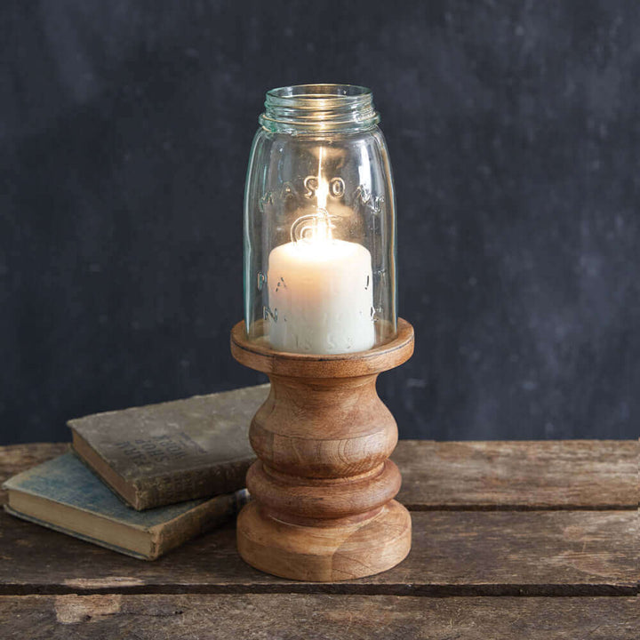 Rustic farmhouse candle holder with Mason jar and lit candle on a wooden base, adding charm to any decor.