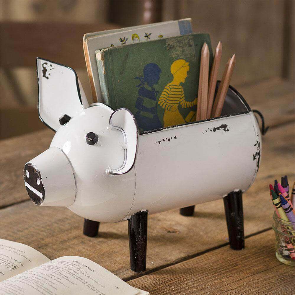 Rustic pig storage organizer with a distressed white finish, holding books and pencils on a wooden table.