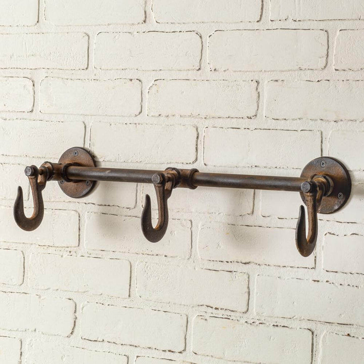 Industrial three hook wall rack in a rustic finish mounted on a white brick wall, ideal for stylish organization.