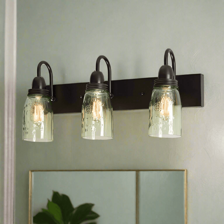 Vintage mason jar wall mounted vanity light with three glass shades on a black metal fixture.